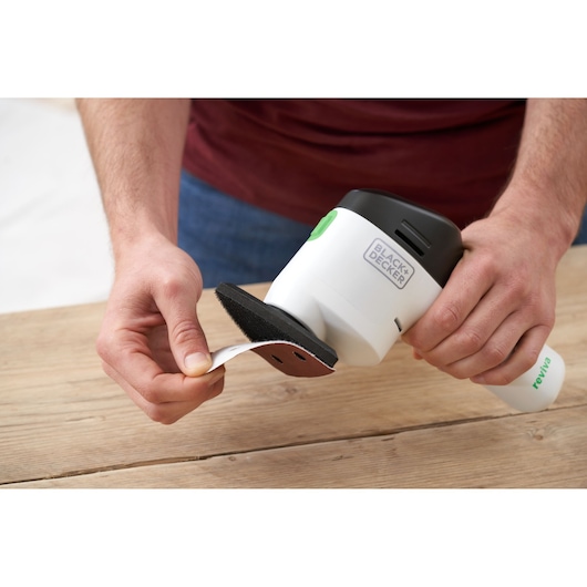 Photo de la ponceuse BLACK+DECKER REVDS12C équipée d'une feuille abrasive, tenue près d'une surface en bois.
