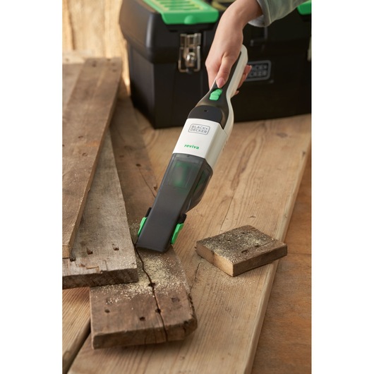 BLACKDECKER REVHV8C handstofzuiger zuigt zaagsel op hout naast gereedschapskist, product in gebruik.