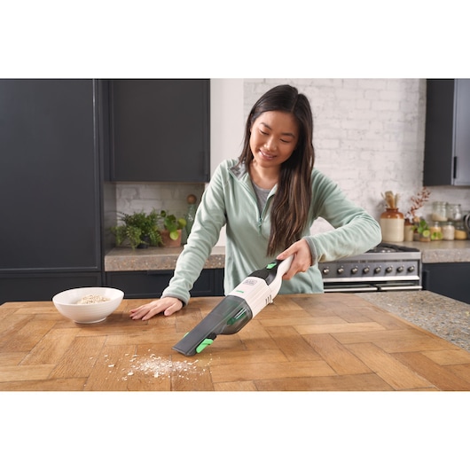 BLACKDECKER REVHV8C handstofzuiger zuigt kruimels op van keukentafel, productfotografie in gebruik.