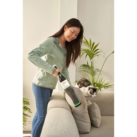BLACKDECKER REVHV8C handstofzuiger reinigt bank, persoon gebruikt apparaat bij kussens en kat.