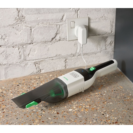 Foto van de witte en zwarte BLACK+DECKER REVHV8C handstofzuiger, oplaadbaar op een aanrecht bij een bakstenen muur.