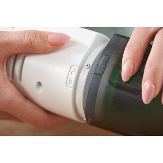 Close-up van de BLACKDECKER REVHV8C handstofzuiger die wordt geopend, handen houden witte behuizing en zwarte stofbak vast.