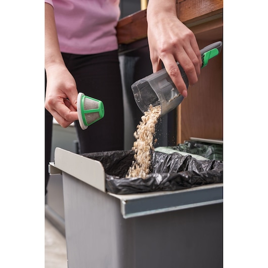 BLACKDECKER REVHV8C handstofzuiger wordt geleegd in prullenbak, persoon houdt filter en stofreservoir vast.