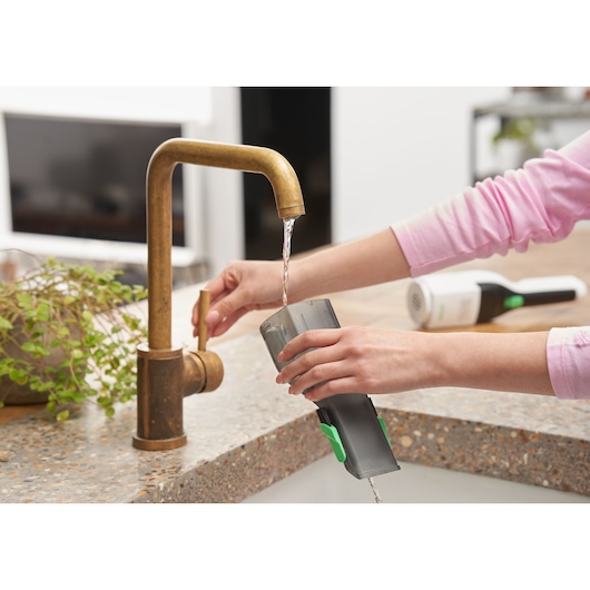BLACK+DECKER REVHV8C handstofzuiger stofreservoir wordt uitgespoeld onder keukenkraan, aanrechtweergave.