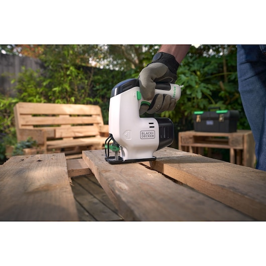 BLACKDECKER REVJ12C decoupeerzaag zaagt hout buiten, met handschoen vastgehouden, tuinmeubels op de achtergrond.