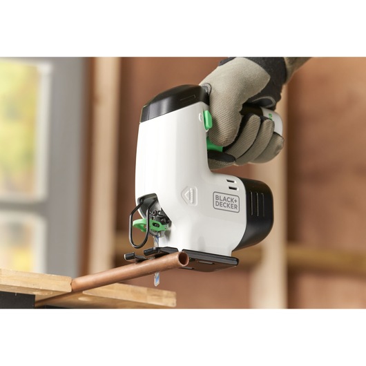 Foto van BLACK+DECKER REVJ12C decoupeerzaag die een koperen pijp zaagt, wit-zwart omhulsel, gehandschoende hand.