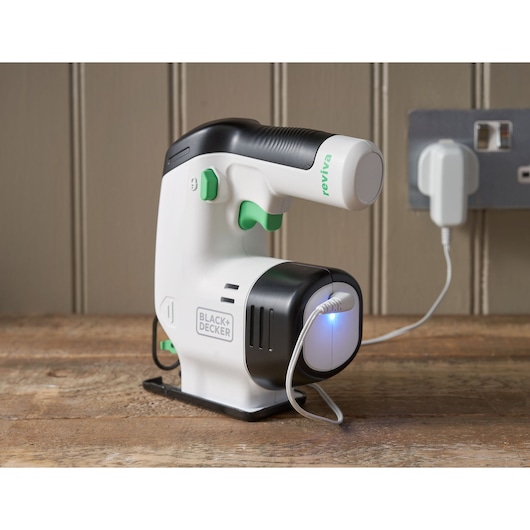 BLACK+DECKER REVJ12C draagbaar wit-zwart textielverzorgingsapparaat met groene accenten, opladend op houten oppervlak.