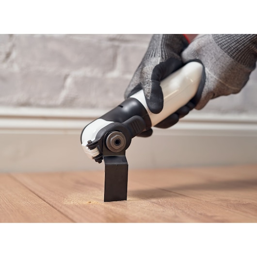 BLACKDECKER REVOS12C multitool snijdt houten vloer, close-up zijaanzicht, gebruiker met handschoenen.