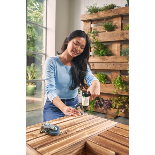 Tournevis sans fil BLACKDECKER REVSD4C utilisé pour fixer une roulette à un meuble en bois en intérieur.