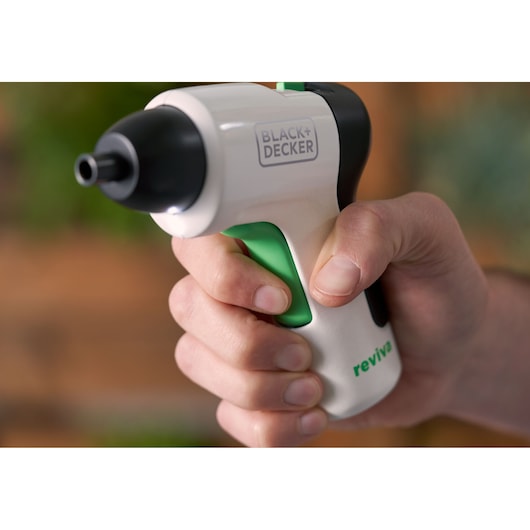 Photo en gros plan du tournevis sans fil BLACK+DECKER REVSD4C dans une main, blanc avec gâchette verte, logo reviva visible.