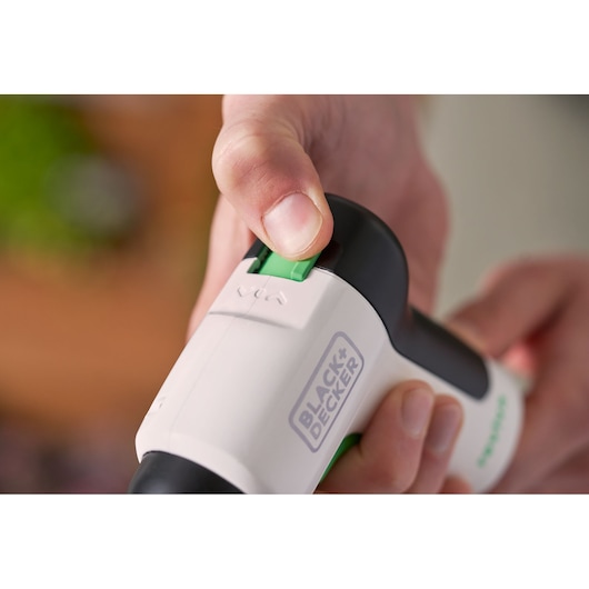 Photo en gros plan d'une main utilisant le tournevis BLACK+DECKER REVSD4C, affichant l'interrupteur vert et le logo.