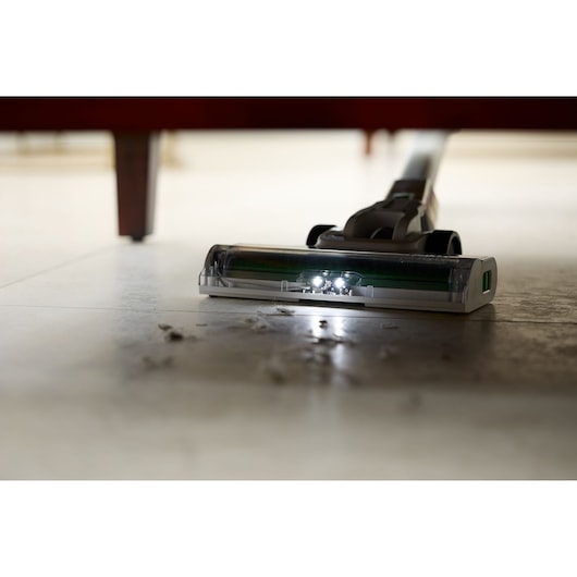 Aspirateur BLACKDECKER REVSV18D1 avec lumières LED nettoyant sous un meuble, vue en contre-plongée, ramasse poussière et débris.
