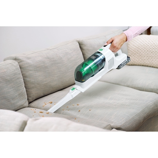 BLACKDECKER REVSV18D1 aspirateur à main avec accents verts nettoyant des miettes sur un canapé, vue latérale.