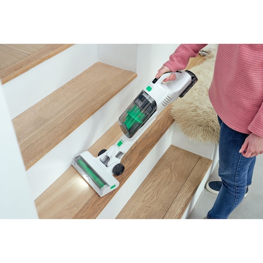 Aspirateur balai sans fil BLACKDECKER REVSV18D1 avec détails verts nettoyant des escaliers en bois.