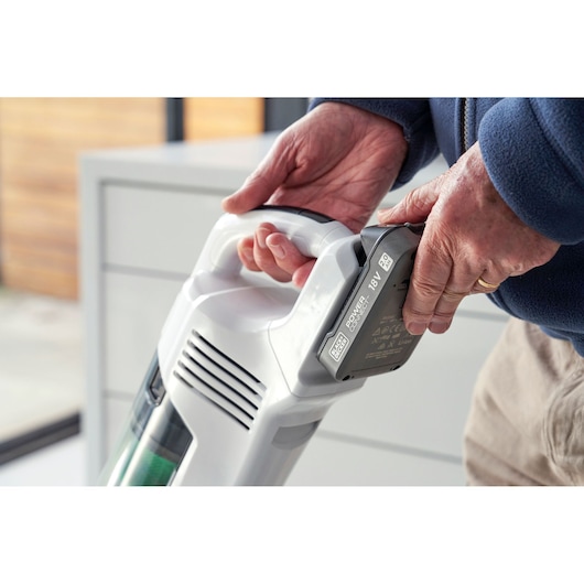 Gros plan de mains fixant une batterie sur un aspirateur sans fil BLACKDECKER REVSV18D1 à l'intérieur.