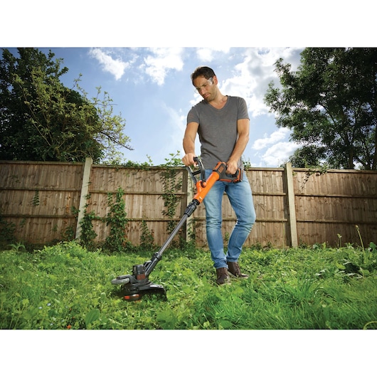 Photo d'une personne utilisant le coupe-bordures sans fil BLACK+DECKER STC1820PC dans un jardin.