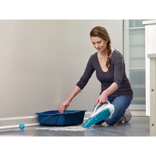 BLACKDECKER WDA315J aspirateur à main nettoyant litière renversée près d’un bac bleu sur sol en carrelage.