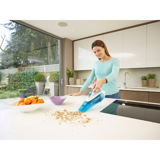 BLACKDECKER WDA315J aspirateur à main nettoyant des miettes sur un comptoir de cuisine blanc près d'une corbeille de fruits.