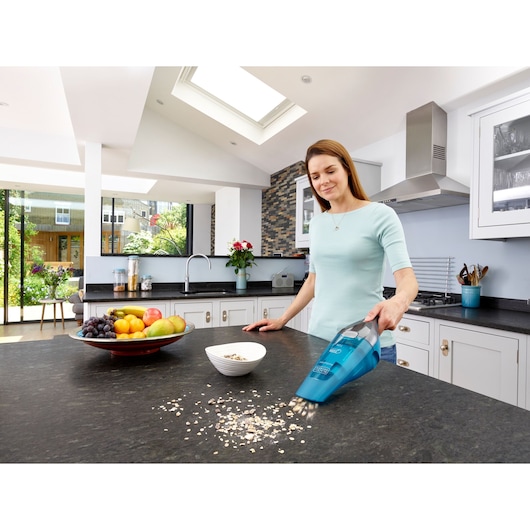 BLACKDECKER WDC215WA aspirateur à main nettoyant des céréales sur le comptoir de la cuisine, bol de fruits visible.