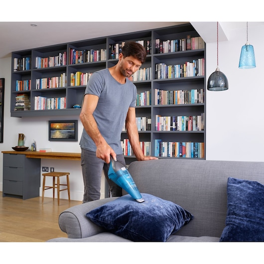 BLACKDECKER WDC215WA aspirateur à main nettoyant un coussin bleu dans un salon moderne.