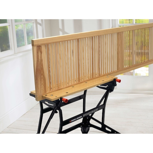 Photo du banc de travail BLACK+DECKER WM626 avec un panneau à lattes en bois fixé dessus, vue latérale en intérieur.