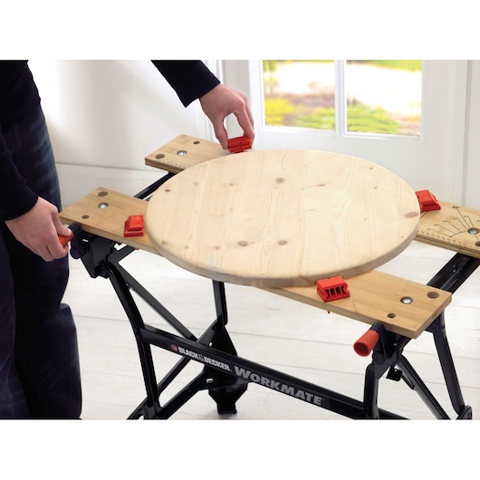 BLACKDECKER WM626 établi pliant avec plateau en bois et pinces rouges, vue de face, tenant une pièce ronde.