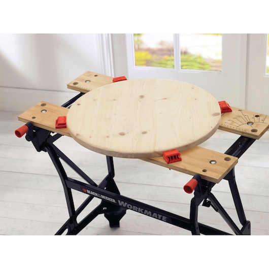 BLACKDECKER WM626 établi tenant une planche ronde en bois avec des serre-joints rouges, intérieur.