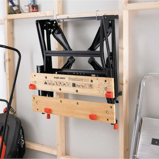 BLACK+DECKER WM626 établi pliant avec plateau en bois et serre-joints orange, monté au mur dans un garage.