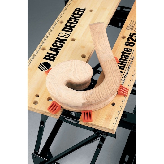 BLACK+DECKER WM825 établi avec pièce en bois et pinces orange, vue de dessus sur fond blanc.